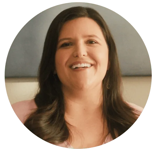 Smiling woman with long dark hair wearing a light pink top, framed in a circular coral background. Represents warmth, encouragement, and Noom’s supportive wellness community.